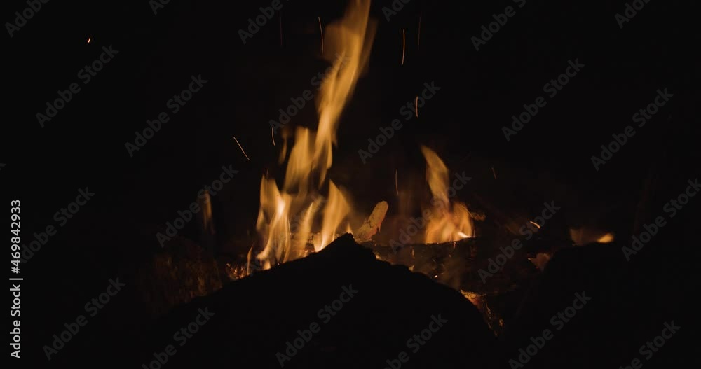 A warm campfire is burning bright at night with the silhouette of rocks in front of it. A warm campfire is burning bright at night with the silhouette of rocks in front of it.