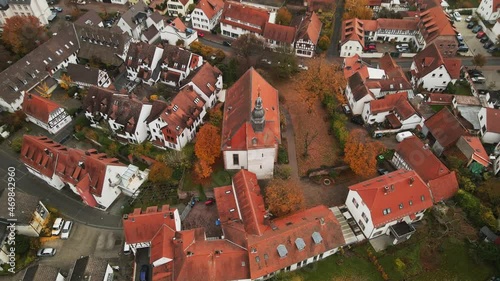 Church with red tile roof in middle of suburb community, Europe. Dietzenbach, Germany. Cinematic aerial pullback photo