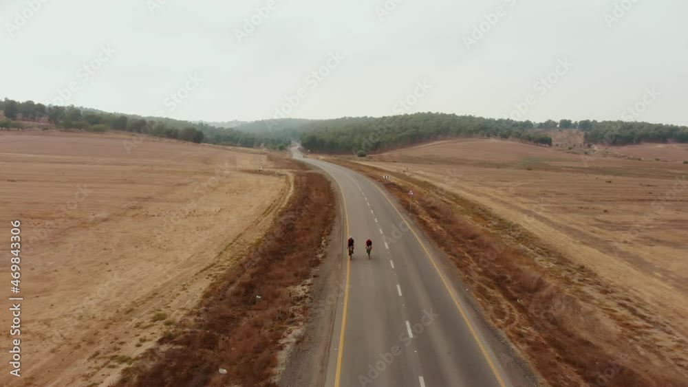 drone aerial shot of the desert's empty road showing the endless horizon and a far forest nirvana while two road bikers approaching. drone aerial shot of the desert's empty road showing the endless horizon and a far forest nirvana while two road bikers approaching.