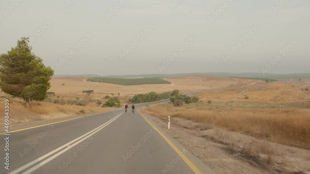 slow motion wide shot of two road cycelist professionals riding in the desert's empty road slow motion wide shot of two road cycelist professionals riding in the desert's empty road
