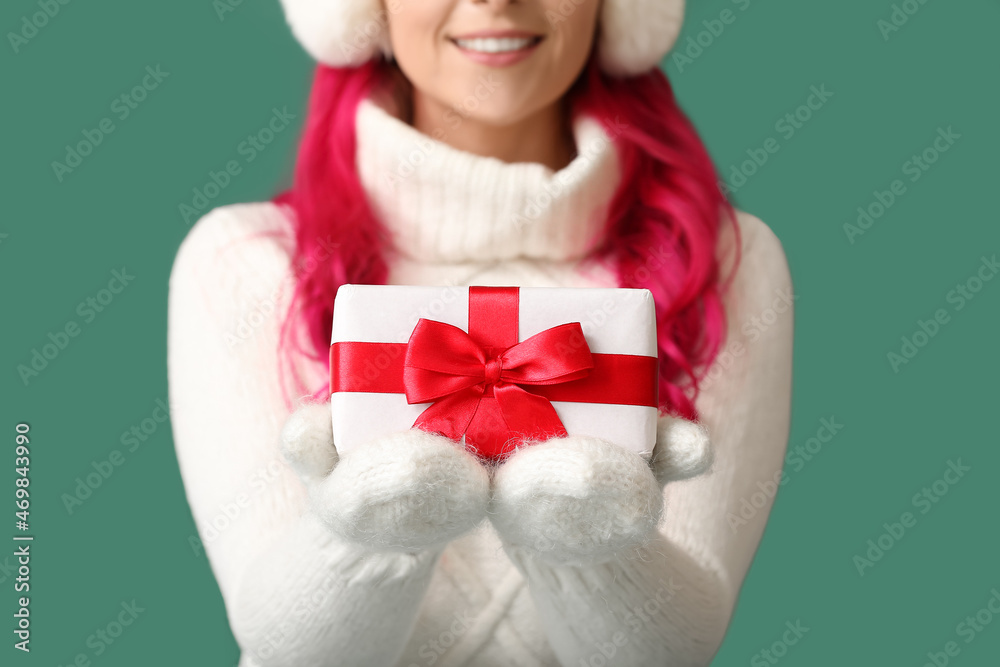 Beautiful woman in warm gloves with Christmas gift on green background, closeup