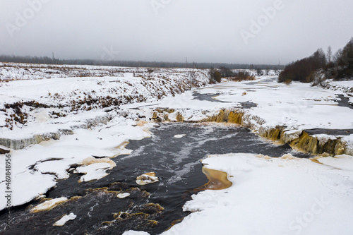 Winter aerial view of the river valley and waterfall. Freezing river. The ice and the banks are covered with snow. Beautiful rural landscape. Cold winter weather. Tosna river, Leningrad region, Russia photo