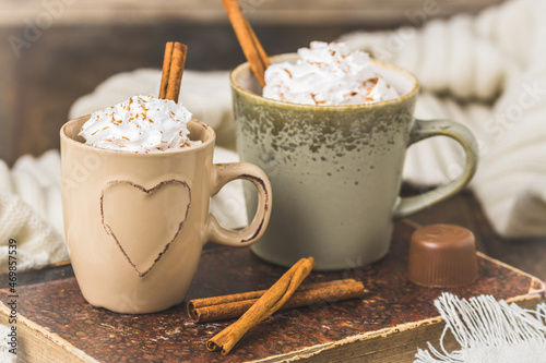 Two cups of coffee or hot chocolate with cream and cinnamon on an old book on wooden background