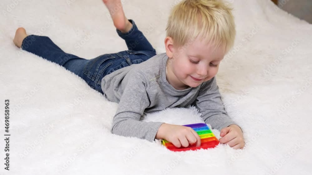 Little boy lies and plays an educational game. Colorful antistress sensory toy fidget push pop it in toddler's hands. Antistress trendy pop it toy. Rainbow sensory fidget. Trendy silicone toy Little boy lies and plays an educational game. Colorful antistress sensory toy fidget push pop it in toddler's hands. Antistress trendy pop it toy. Rainbow sensory fidget. Trendy silicone toy