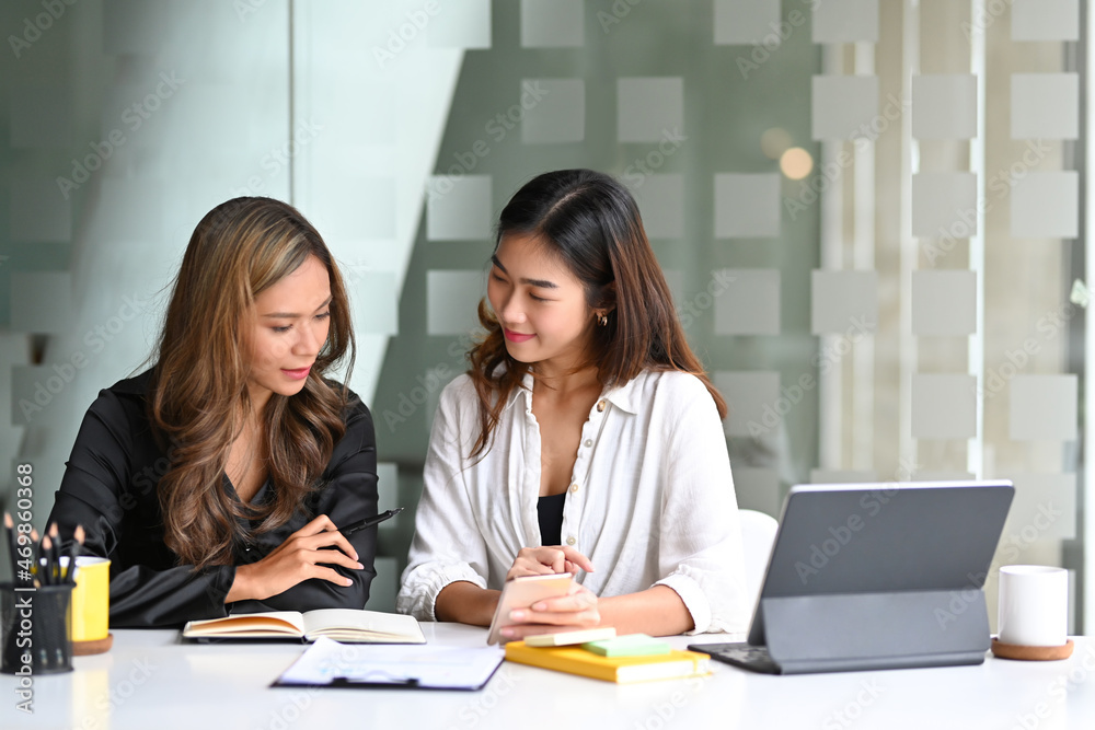 Two businesswomen sitting at office desk and talking about project startup ideas. Two businesswomen sitting at office desk and talking about project startup ideas.