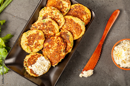 Turkish style zucchini pancakes or fritters known as mucver, served on black plate with fresh greens and sour cream. Close up image on dark stone background. photo