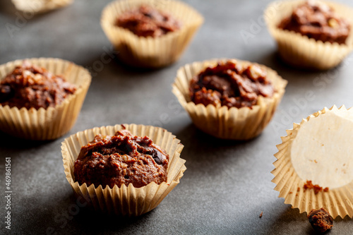 Shallow depth of field angled view of chocolate and nut muffins in liner papers fresh out of oven. Dark background moody low light image. Crumbles on stone background