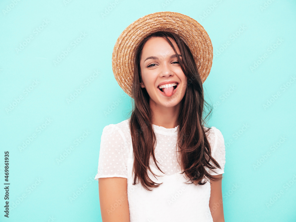 Closeup portrait of young beautiful smiling female in trendy summer dress.Sexy carefree woman posing near blue wall in studio.Positive model having fun indoors.Cheerful and happy in hat. Shows tongue Closeup portrait of young beautiful smiling female in trendy summer dress.Sexy carefree woman posing near blue wall in studio.Positive model having fun indoors.Cheerful and happy in hat. Shows tongue