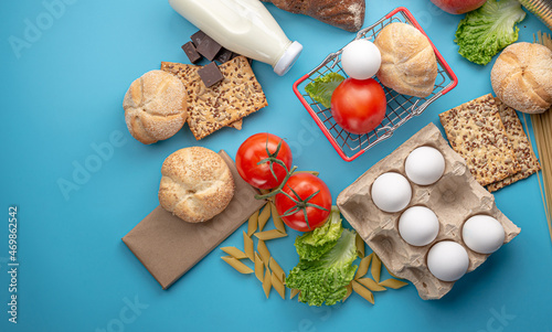 Set of fresh products and a miniature shopping basket on a blue background top view. Online shopping concept, food delivery