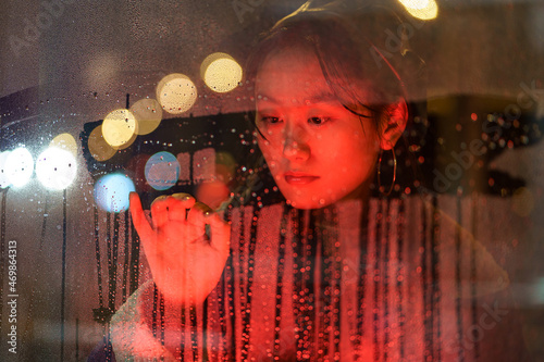 Fotografie Sensitive asian millennial girl suffer from solitude alone draw on wet glass in rain