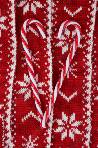 Heart shape made of candy cane ornaments on red and white knitted wool background. Christmas festive background