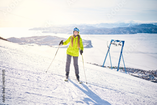 Cheerful skier girl in green jacket in front of snowy mountains and pacific ocean