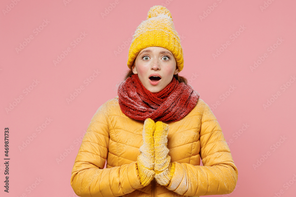 Shocked surprised young woman 20s years old wears yellow jacket hat mittens holds hands folded in prayer gesture begging about something isolated on plain pastel light pink background studio portrait. Shocked surprised young woman 20s years old wears yellow jacket hat mittens holds hands folded in prayer gesture begging about something isolated on plain pastel light pink background studio portrait.