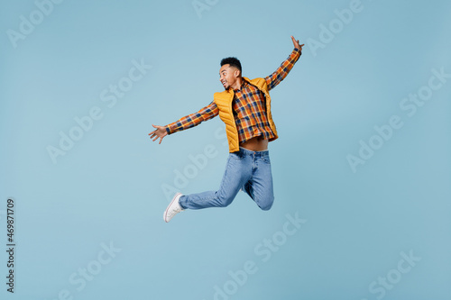 Full size body length overjoyed excited jubilant fun young black man 20s years old wear yellow waistcoat shirt jump with spreading hands isolated on plain pastel light blue background studio portrait