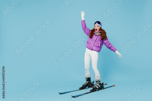 Full body skier beginner fun cool woman wearing warm purple padded windbreaker jacket ski goggles mask spend extreme weekend in mountains skiing leaning back isolated on plain blue background studio photo