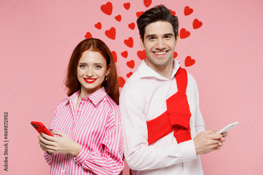 Young couple two friends woman man wearing casual shirt using hold in hand mobile cell phone isolated on plain pastel pink background studio portrait. Valentine's Day birthday holiday party concept Young couple two friends woman man wearing casual shirt using hold in hand mobile cell phone isolated on plain pastel pink background studio portrait. Valentine's Day birthday holiday party concept
