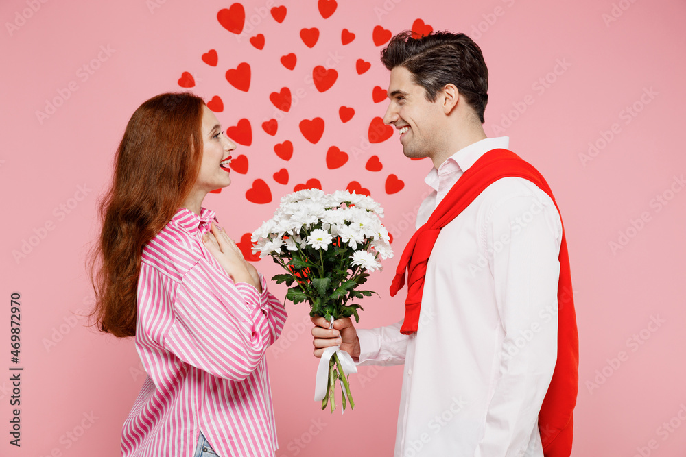 Side view young thankful happy couple two friends woman man 20s in casual shirt hold bouquet of flowers isolated on plain pastel pink background studio. Valentine's Day birthday holiday party concept. Side view young thankful happy couple two friends woman man 20s in casual shirt hold bouquet of flowers isolated on plain pastel pink background studio. Valentine's Day birthday holiday party concept.