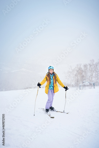 Portrait of cheerful skier girl in yellow jacket in a snowy weather