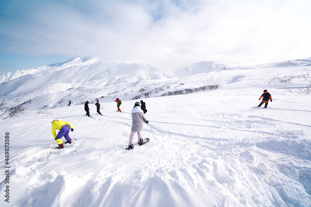 Group of snowboarders freeriding in front of snowy mountains and blue sky