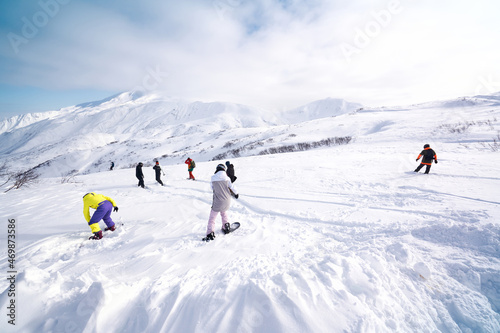 Group of snowboarders freeriding in front of snowy mountains and blue sky