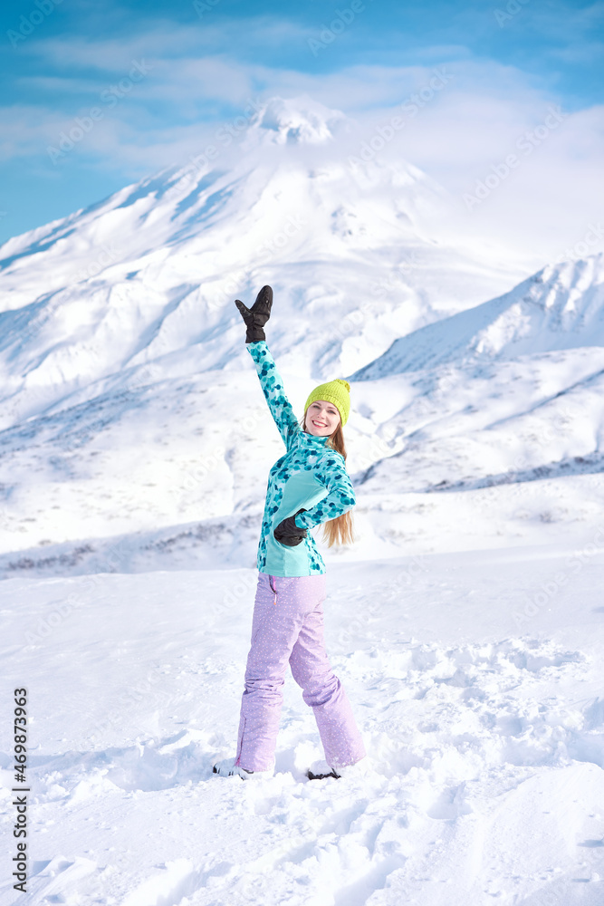 Cheerful girl snowboarder in blue sweater in front of snowy mountains and blue sky