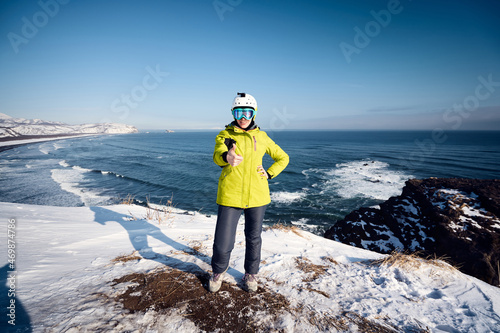 Young tourist woman in a green jacket looking at camera at the edge of the Pacific ocean. Kamchatka peninsula, Russia