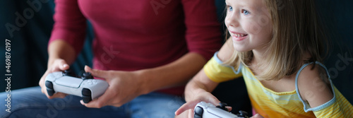 Little girl and mother sitting on couch and holding computer joysticks in their hands