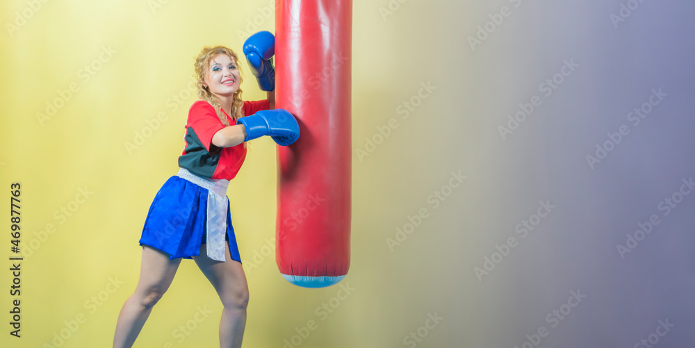 Young and beautiful girl, mixed martial arts fighter, strikes punching bag with her hand. Looks into camera. Young and beautiful girl, mixed martial arts fighter, strikes punching bag with her hand. Looks into camera.