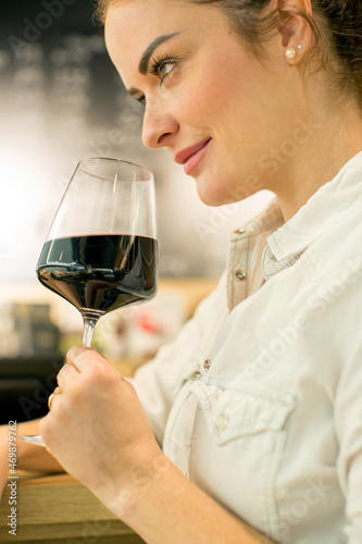 Young attractive woman, tasting wine in a wine store, enjoying glass of tasty wine