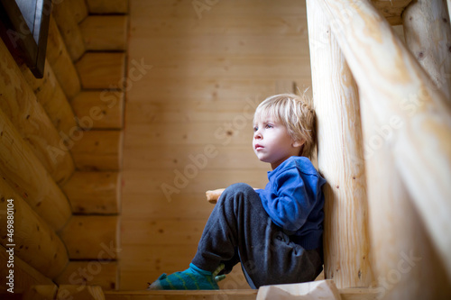 Little cute blond toddler child, sitting on a stairs in a wooden cabin, drinking milk
