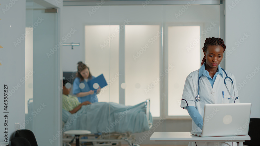 Obraz premium Physician working with technology on modern laptop in hospital ward. Medical specialist using gadget to work on healthcare system, helping sick patient with treatment and medicine.