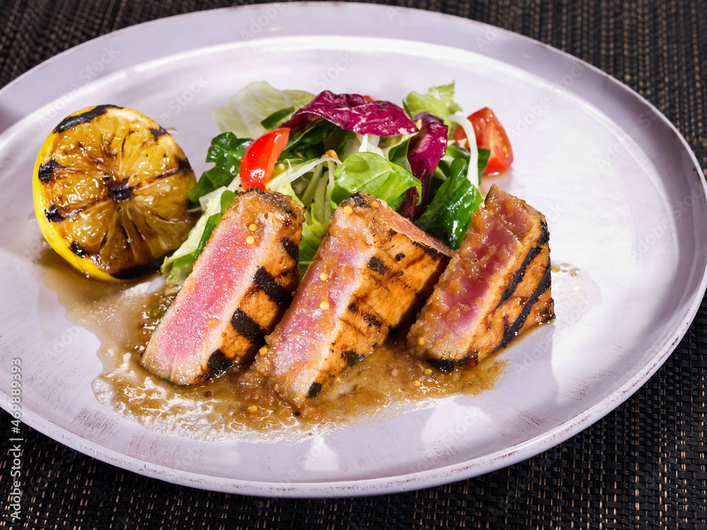 grilled tuna fillet served with salad mix and grilled lemon on a plate on dark background grilled tuna fillet served with salad mix and grilled lemon on a plate on dark background