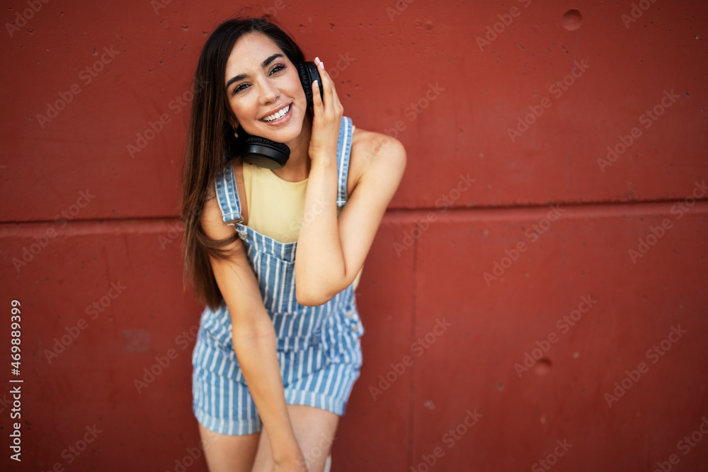 Fototapeta premium Young happy woman listening to music outdoors. Positive hipster girl with headphones enjoying in sunny day..