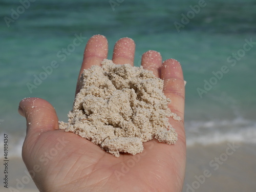 A woman's hand holds a handful of fine white sand against the background of ocean waves on a sunny summer day on a summer vacation.