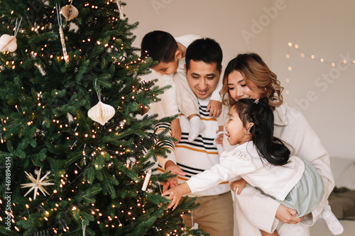 A happy diverse Asian family celebrates Christmas. Parents with children give gift boxes decorate the Christmas tree and prepare for the New Year holiday in a decorated house. Selective focus