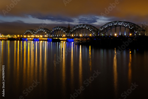 Reflection of night lights at dawn on the Daugava in Riga against the background of the railway bridge
