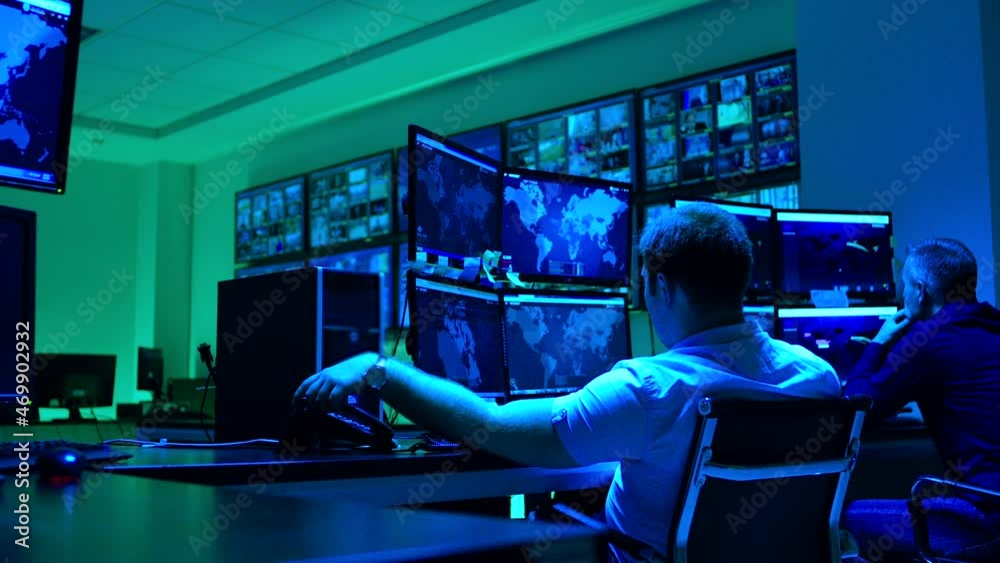 Male workers sitting near computers on monitoring room and working . Programmers or engineers using many laptops , computers , searching , following information and statistics . Cyber security office 