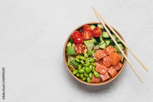 Salmon, avocado, cucumber, tomato, edamame beans and rice poke bowl on light gray background