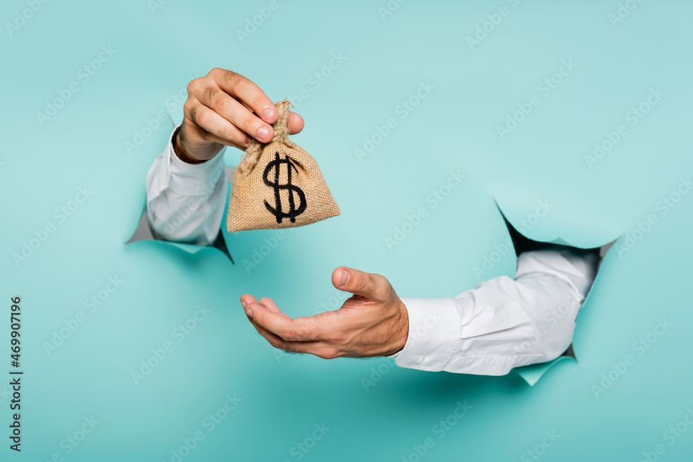 partial view of man holding money bag with dollar sign through holes in paper wall on blue Stock Foto Adobe Stock