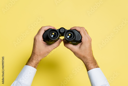 cropped view of man holding black binoculars in hands on yellow