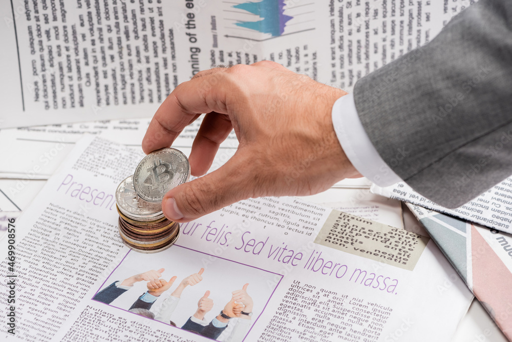 Naklejka premium KYIV, UKRAINE - NOVEMBER 1, 2021: cropped view of man holding bitcoin near printed newspaper with lettering, translation: free life but risky