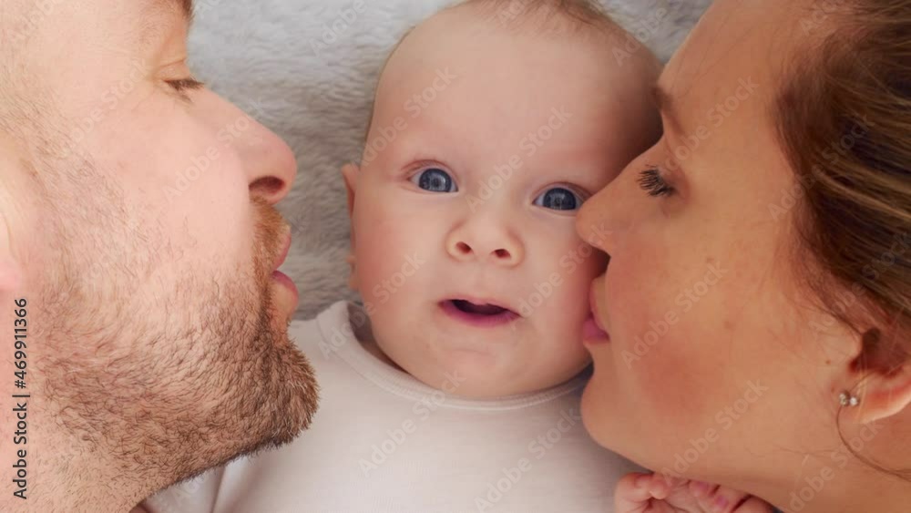 Happy parents kissing his newborn baby with, top view. Happy family. Healthy newborn baby with mom and dad. Close up Faces of the mother, father and infant baby. Cute Infant boy and parents. Happy parents kissing his newborn baby with, top view. Happy family. Healthy newborn baby with mom and dad. Close up Faces of the mother, father and infant baby. Cute Infant boy and parents.