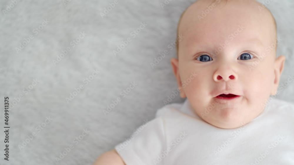 Child's face of a Happy newborn baby looking to camera. Healthy newborn baby in a white t-shirt with blue eyes. Slow motion. Face of a Beautiful active tiny child. Cute white Infant boy, top view. Child's face of a Happy newborn baby looking to camera. Healthy newborn baby in a white t-shirt with blue eyes. Slow motion. Face of a Beautiful active tiny child. Cute white Infant boy, top view.