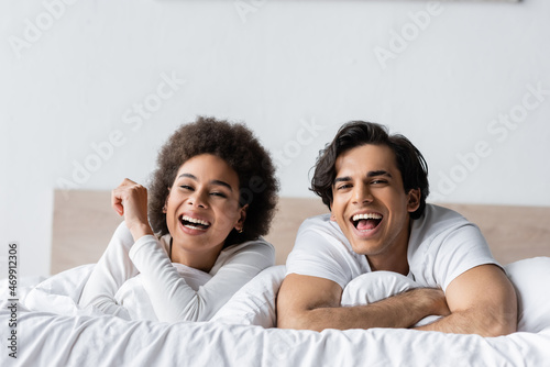 happy multiethnic couple laughing while lying in bed