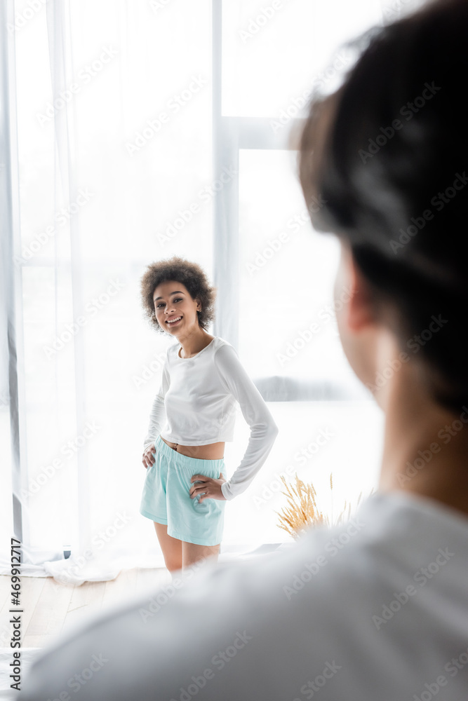 happy african american woman standing with hands on hips while looking at blurred boyfriend happy african american woman standing with hands on hips while looking at blurred boyfriend