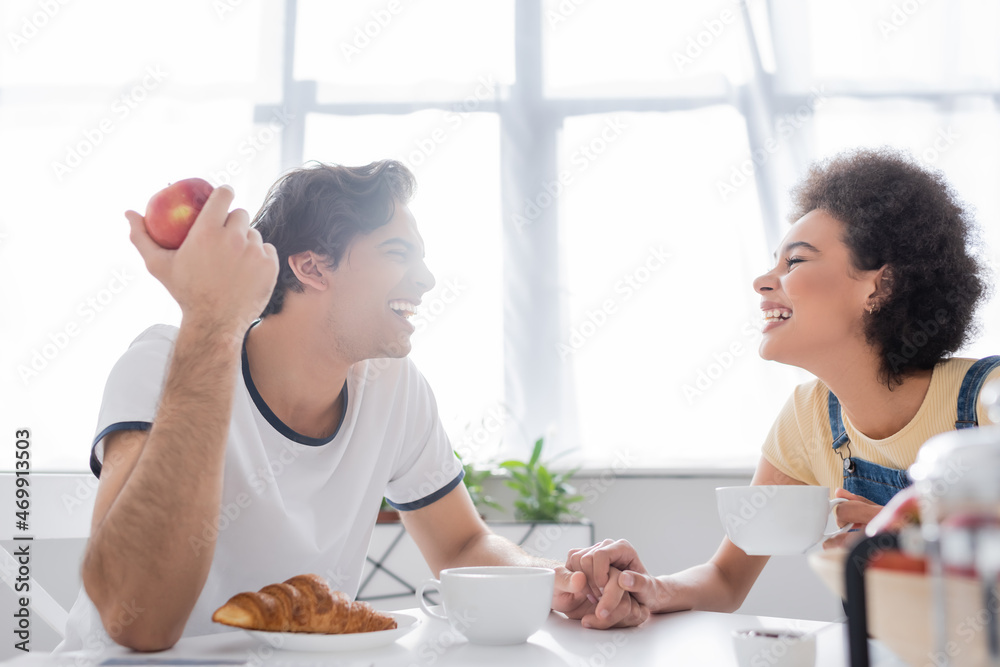 side view of happy multiethnic couple holding hands during breakfast side view of happy multiethnic couple holding hands during breakfast