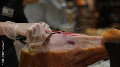 a chef in a dark apron and white gloves cuts a slice of ham from a pork leg in a restaurant. the chef cuts a slice of jamon close-up photo