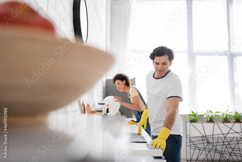 young man cleaning kitchen cabinet with rag near curly african american woman in kitchen
