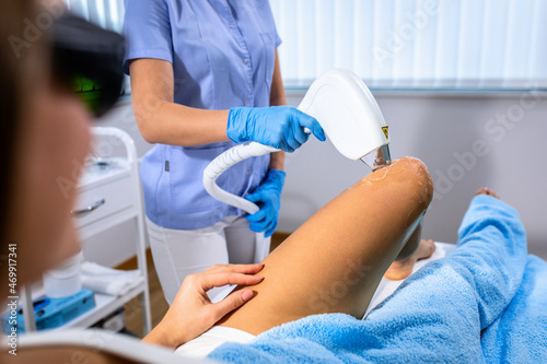 Woman in a beauty salon removes hair from her leg with laser epilation.