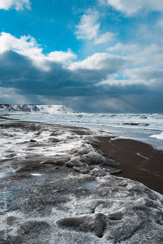 Winter landscape with frozen sea and icy beach. Storm and snow weather. Dramatic seascape.